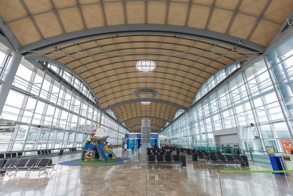 Spacious waiting area inside Alicante Airport with seating, glass walls and children’s play area