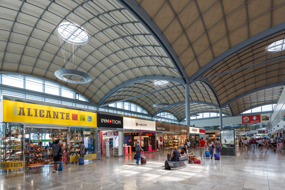 Shopping area inside Alicante Airport with souvenir stores, retail shops and passengers in the terminal
