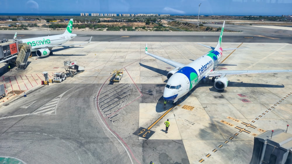 Planes parked at Alicante Airport gates with runway and coastline views in the background