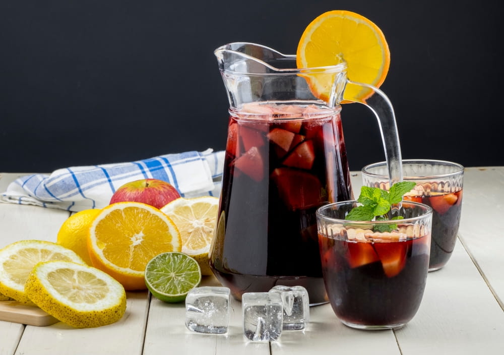 Jarra y copas de sangría roja en España con naranja, limón, lima, manzana, menta y hielo