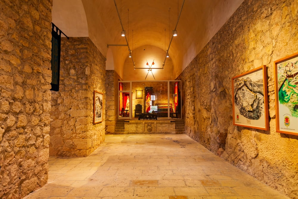 Interior exhibition hall inside Santa Barbara Castle in Alicante with stone walls and historical maps