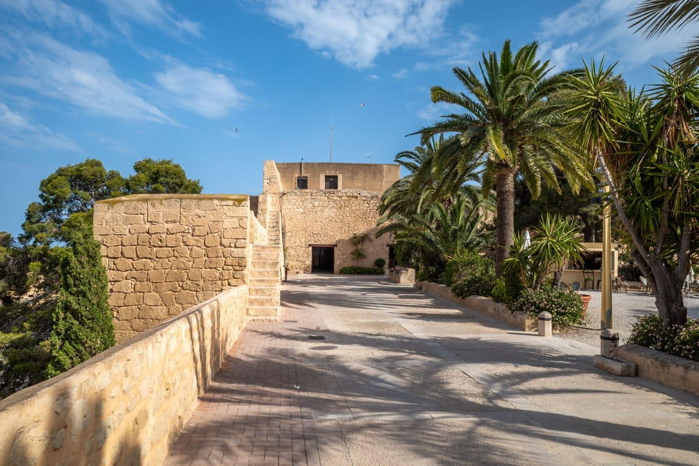 Entrance area inside Santa Barbara Castle in Alicante with stone walls and palm trees