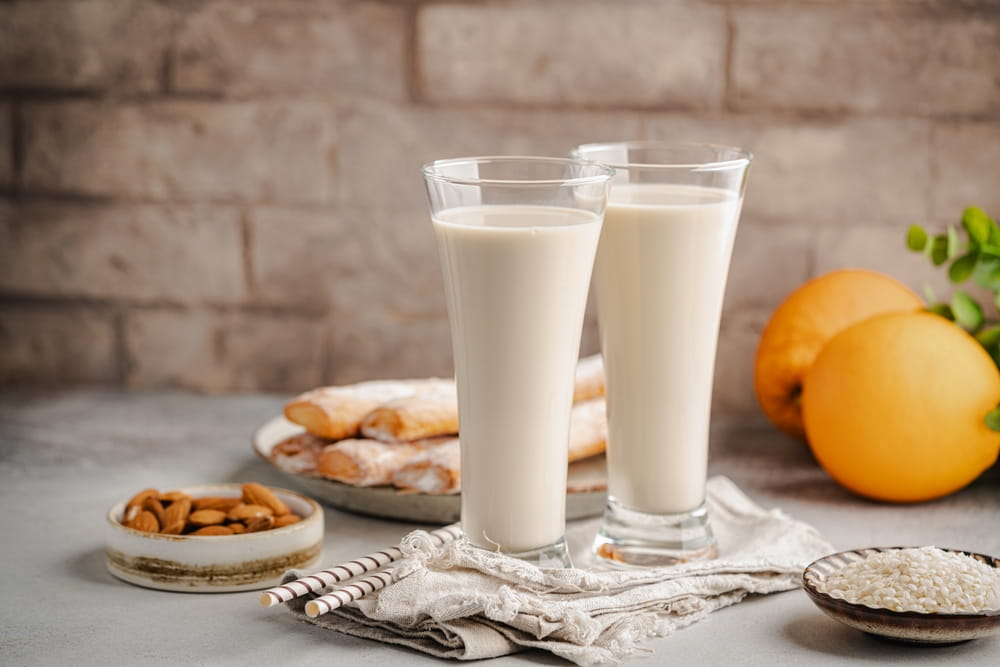 Two glasses of horchata in Spain with pastries, almonds, rice and oranges on a table.