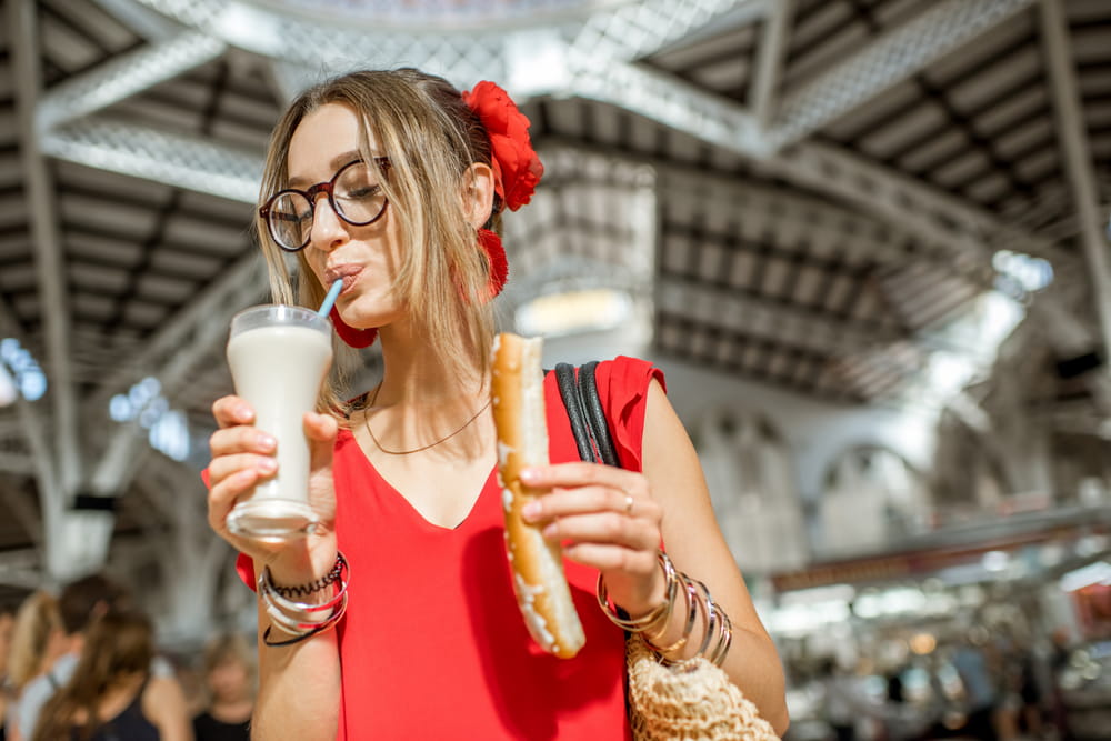 Mujer bebiendo horchata in Spain mientras sostiene un fartón en un mercado tradicional.